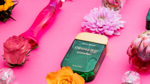 Avroy Shlain perfume bottle surrounded by pink flowers and glass ornaments on a pink background