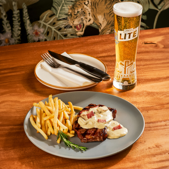 Steak and chips with a Castle Lite beer on a restaurant table at Piatto