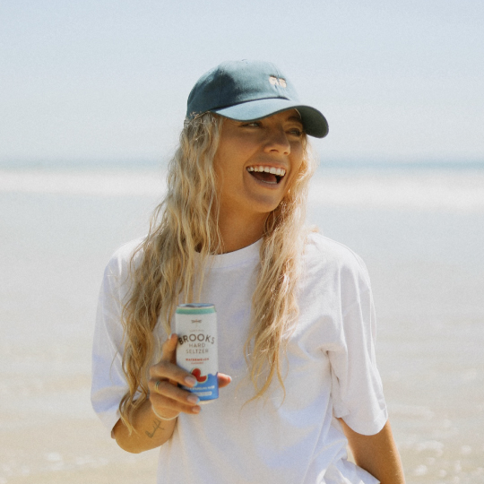 Woman laughing on a beach holding a can of Brooks Hard Seltzer